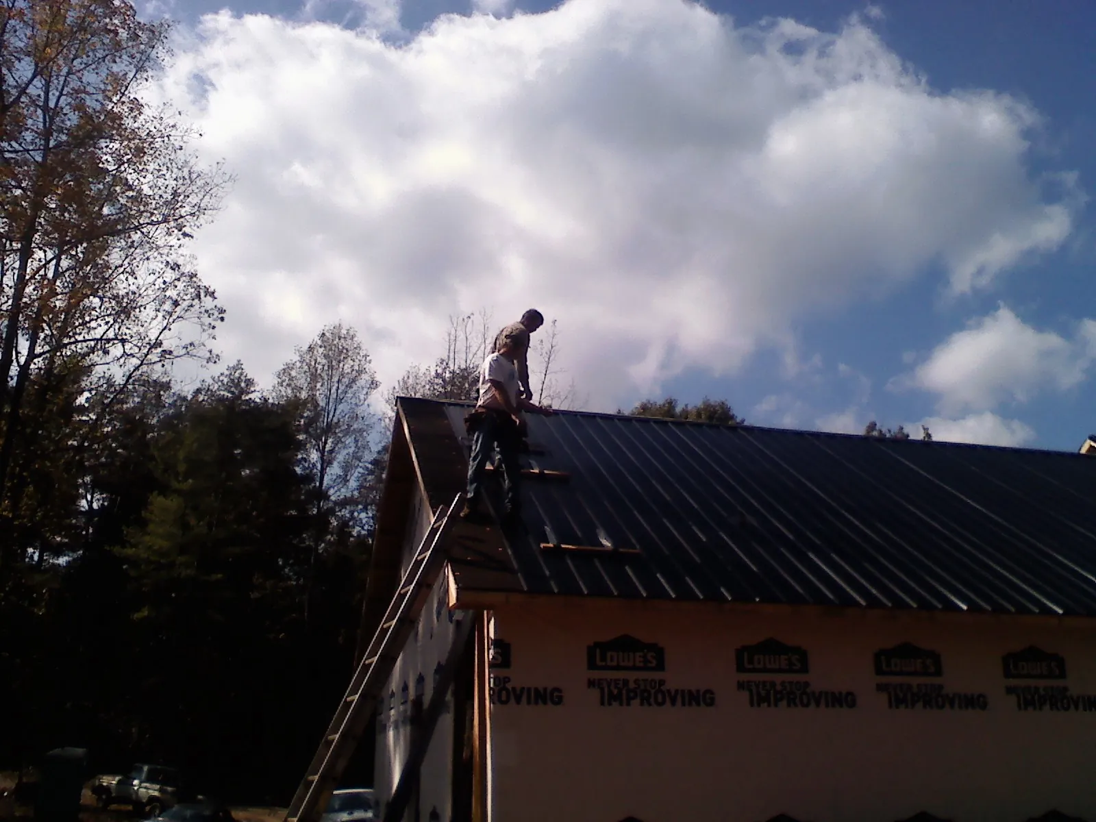 Roofer fastening dark metal panels high against a cloudy sky, from a Roof Inspection job in Seaside Heights