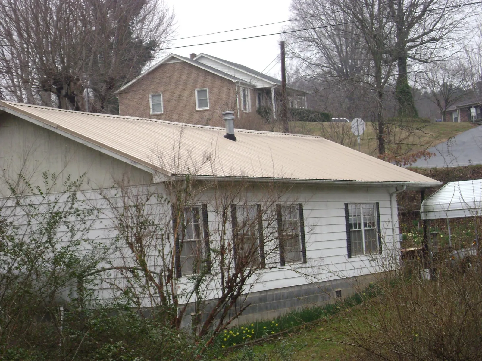 Tan metal roof on a white sided house set into a hillside — Commercial Roofing by Roofing Brothers in Seaside Heights